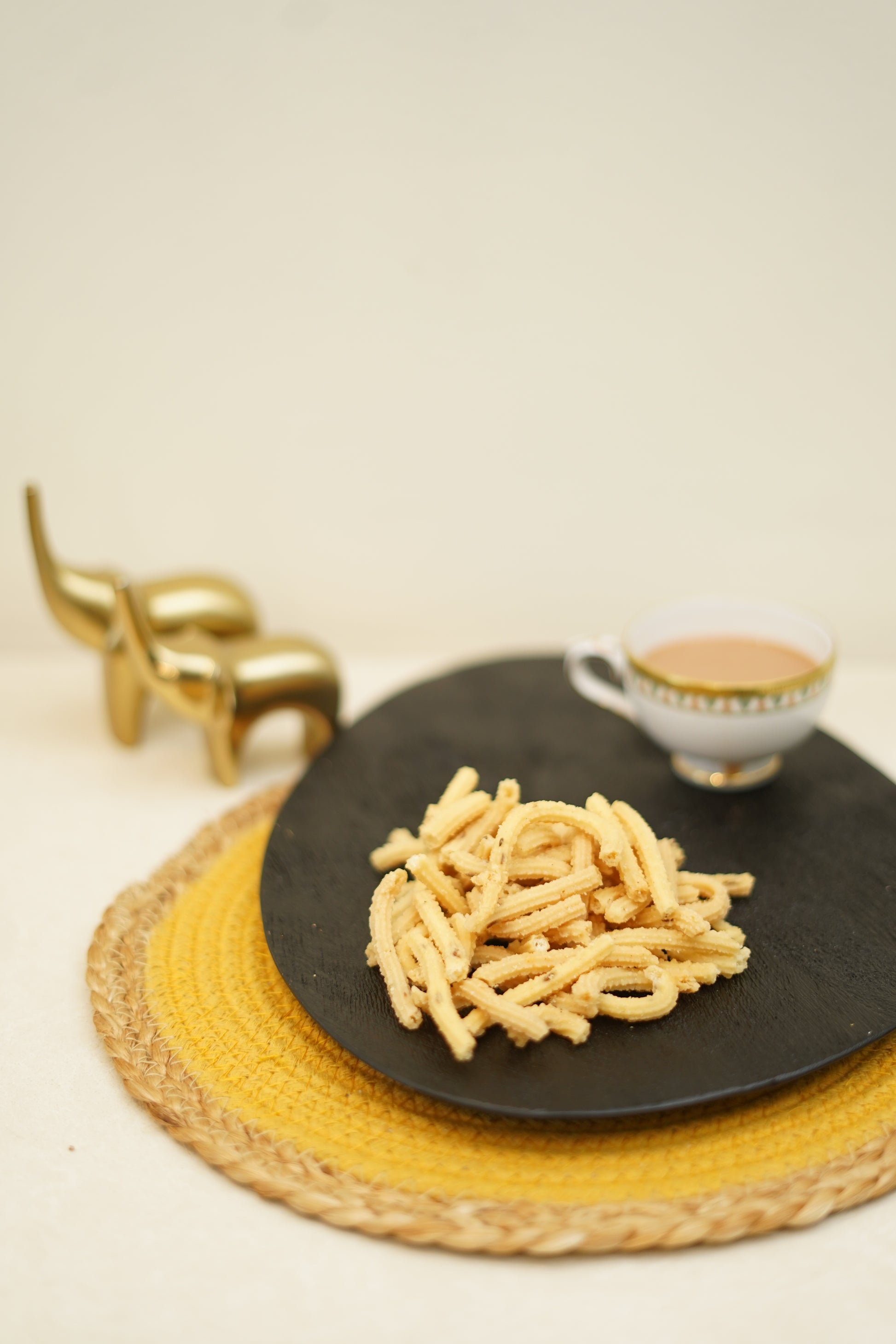 A plate of crispy rice sticks served with a side of dip, presented on a black plate with a decorative golden object in the background.