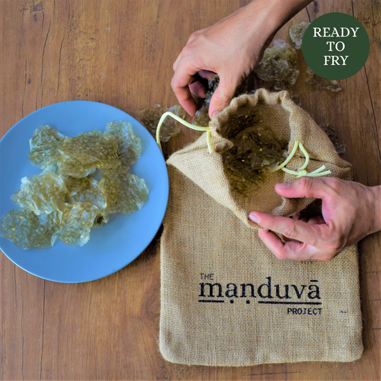 Person opening a burlap bag labeled 'The Manduva Project' with fried food on a blue plate beside it.